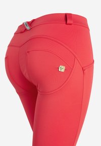Leggings rossi con un design aderente, tessuto elasticizzato, dettagli cuciti distintivi e un piccolo logo dorato sulla tasca posteriore.