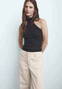 Black ribbed sleeveless top with a high neckline paired with cream wide-leg pants featuring front and back pockets and a button closure.