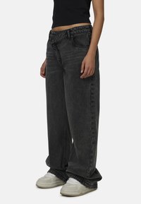 Czarne luźne dżinsy o wyblakłej fakturze, wysoki stan, proste nogawki, zestawione z białymi trampkami. Brak widocznych wzorów lub akcentów.