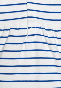 Vitt tyg med horisontella blå ränder, prytt med tryckknappar och rynkade veck nära mitten.