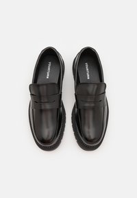 Black leather loafers with a smooth finish, featuring a decorative strap and flat soles, designed for casual wear. Interior has branded cushioning.
