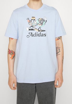 Jasnoniebieska koszulka Adidas z kreskówkową kredką w kapeluszu oraz uśmiechniętą kulą ziemską pokazującą znak pokoju nad nazwą marki.