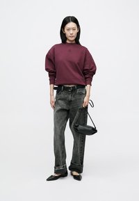 Finstubrød oversized sweatshirt, grå vide jeans, svarte flate sko og en liten svart håndveske. Glatt stoff, avslappet passform og oppbrettede jeans.