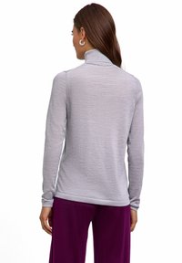 Maglione a collo alto grigio chiaro a maniche lunghe con una texture morbida e un design aderente, abbinato a pantaloni viola larghi.