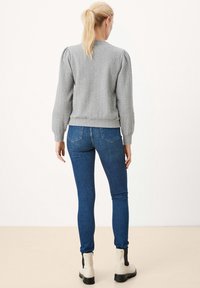 Grauer, strukturierter Pullover mit Fischgrätenmuster, Rundhalsausschnitt und puffigen Ärmeln, kombiniert mit blauen Skinny-Jeans und weißen Stiefeletten.
