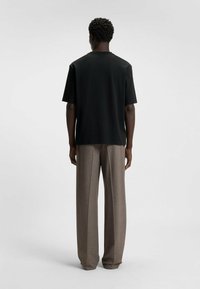Black short-sleeve t-shirt made of a smooth fabric, paired with loose-fitting, brown textured trousers. Back view highlights simplicity in design.