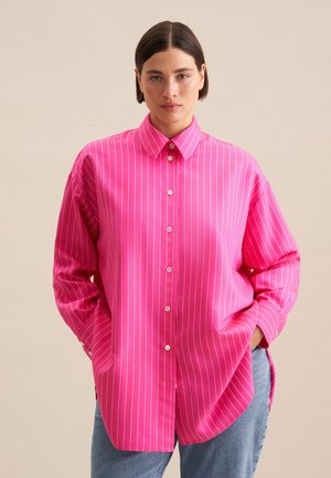 Lys pink skjorte med knapper og hvide lodrette striber, der har en klassisk krave, lange ærmer og en afslappet pasform. Casual denim bukser.