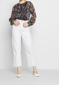 Blus med blommönster och puffärmar i marinblått, rosa och krämfärgat, kombinerad med högmidjade vita raka jeans och vita klackar.