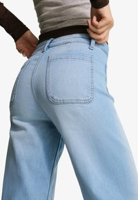 Svetlo modre kavbojke iz jeansa z visokim pasom, zadnjimi žepi in ohlapnim krojem. Tkanina ima gladko teksturo in minimalne šive.