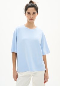Světle modré oversized tričko vyrobené z měkké látky. Má kulatý výstřih a krátké rukávy, s volným střihem a minimem švů pro pohodlí.