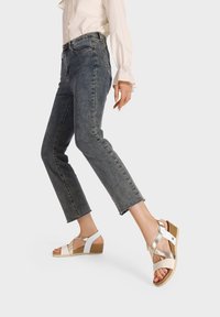 Sandali con zeppa caratterizzati da una combinazione di cinturini bianchi e dorati, suola in sughero, lavorazione tessuta sulla parte superiore e design con punta aperta.