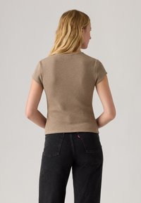 Top de manga corta de color marrón claro y con relieve, de diseño ajustado, combinado con unos jeans negros de cintura alta que presentan costuras en contraste y detalles de logo.