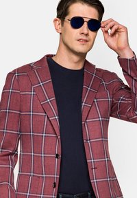 Czerwono-granatowa marynarka w kratę z teksturowanej tkaniny, z klapami w kształcie notcha i dwoma guzikami, zestawiona z granatową koszulą i okularami przeciwsłonecznymi.