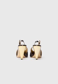 Tacchi slingback in pelle patent marrone con punta affilata e caratteristico tacco a cono dorato. Presentano una cinghia alla caviglia e lati aperti.