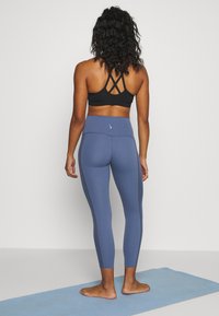 Top sportivo nero con design a incrocio sulla schiena abbinato a leggings blu con cuciture laterali decorative. Finitura opaca, stile aderente.