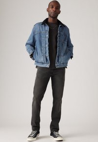 Denimjakke med svart faux fur-krage, lyseblå farge, frontknapper og sidelommer. Båret over en svart skjorte og kombinert med mørke jeans.