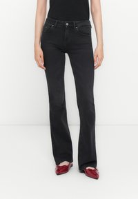 Jeans évasés noirs en denim, dotés de cinq poches, d'une fermeture à bouton et d'une finition légèrement délavée. Portés avec des ballerines rouges à bout pointu.