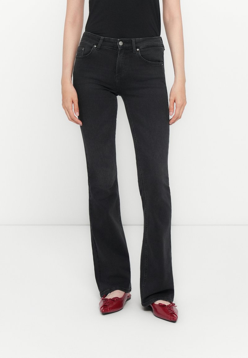 Jeans évasés noirs en denim, dotés de cinq poches, d'une fermeture à bouton et d'une finition légèrement délavée. Portés avec des ballerines rouges à bout pointu.