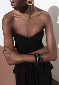 Black strapless dress with ruched texture, layered ruffles at the hem, and gold-tone hoop earrings. Accessorized with stacked bracelets.
