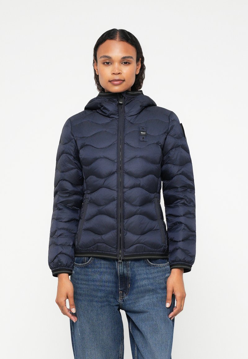 Tumši zils pūkainais apmetnis ar quilted dizainu, kapuci un priekšējo rāvējslēdzēju. Aprīkots ar mazu logotipu uz krūšu un ribotām piedurknēm.