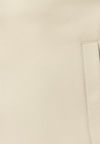 Tissu beige texturé avec une ouverture de poche rectangulaire surpiquée sur le côté droit.