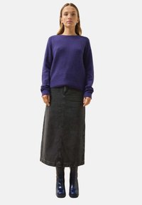 Lila gerippter Pullover mit hohem Kragen, langen Ärmeln; schwarze Denim-Maxiröcke; glänzende marineblaue Absatzstiefel. Saubere, minimalistische Präsentation.