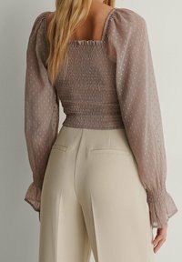 Skirtrad topp i mjuk taupe med genomskinliga, prickiga långärmar; ihopparad med högmidjade, krämfärgade byxor med sidofickor.