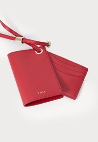 Red leather cardholder with a textured finish, gold hardware, and a strap. Features multiple card slots and a brand logo at the bottom.