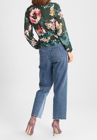 Fladdrande mörkgrön blus med blommig mönstring i rosa, vitt och teal, kombinerad med högmidjade ljusblå jeans och ljusrosa klackar.