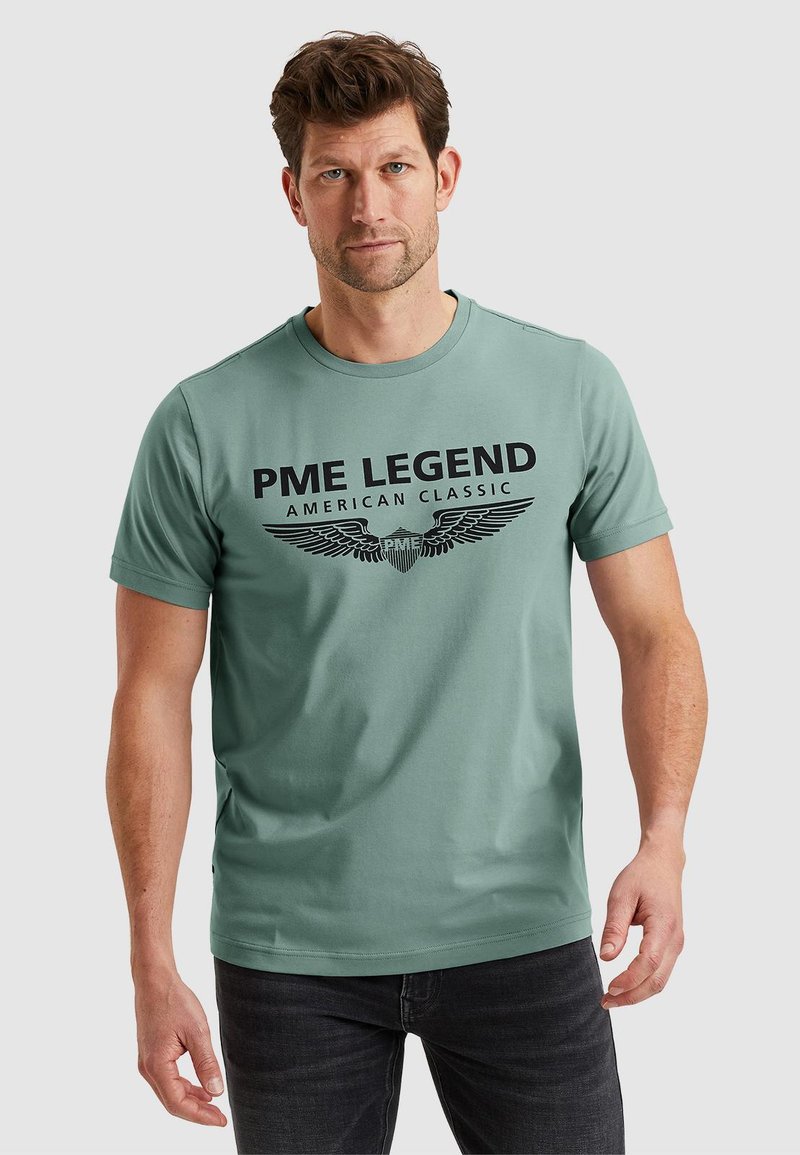 Light green short-sleeve t-shirt made from soft fabric, featuring a bold black graphic text and wings design on the front.