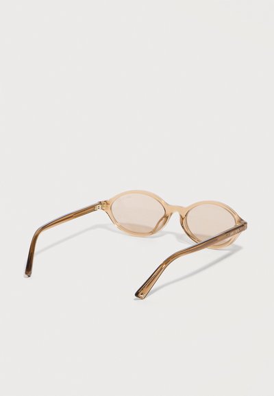 Στρογγυλά γυαλιά ηλίου με μπεζ απόχρωση και λεπτά διαφανή καφέ πλαίσια, ανοιχτά και ακουμπισμένα σε λευκή επιφάνεια.
