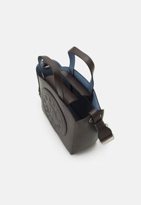 Bruine leren handtas met een gestructureerd ontwerp, voorzien van een rond geperst logo, een blauwe binnenkant en dubbele bovenhandvatten met een afneembare riem.