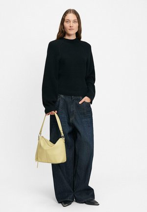 Schwarzer gerippter Pullover mit langen Ärmeln, kombiniert mit lockeren dunkelblauen Jeans. Hält eine glatte gelbe Lederhandtasche mit geschwungener Form.