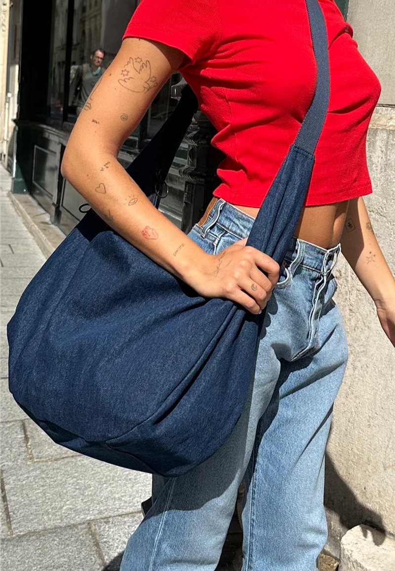 Mörkblå denim axelväska med en avslappnad, överdimensionerad design. Mjuk textur, bred rem och samlad kropp för en avslappnad stil.