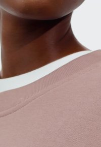 Felpa rosa chiaro con finitura testurizzata, dotata di colletto a coste bianco e dettagli di cucitura puliti. Primo piano della scollatura.