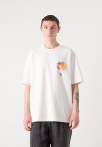 Hvit oversized bomulls T-skjorte med et fargerikt oransje grafikkmotiv på venstre bryst og logotekst under. Korte ermer, rund hals.