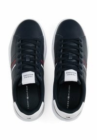 Granatowe sneakersy z gładką syntetyczną cholewką, białą podeszwą, czarnymi sznurówkami, czerwono-białymi paskami oraz markowym językiem i wkładką.