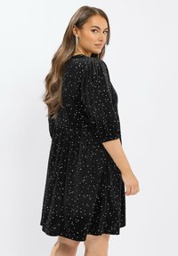 Schwarzes Samtkleid mit Puffärmeln, tailliertem Bund und verstreuten silbernen Sternmustern. Der schwingende Rock reicht bis zur Mitte des Oberschenkels.