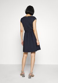 Námořnické modré šaty s krátkými rukávy, kulatým výstřihem, přiléhavým pasem a rozšířenou sukní. Nosí se s vysokými sandály se zebřími pruhy.