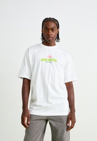 Hvid bomulds t-shirt med et farverigt "Expedition Series" grafisk logo, korte ærmer og en afslappet pasform. Paret med grå jeans.