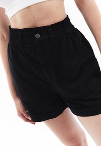 Pantaloni corti neri in cotone con vita elastica e chiusura con bottone, tasche laterali e orlo arrotolato per un fit rilassato.