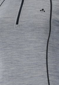 Harmaa neule takki, jossa on teksturoitu pinta, puolivälin vetoketjukaulus, musta korostusommel ja pieni logo yläosassa.