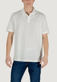 Polo bianco con un motivo testurizzato, maniche corte e colletto classico. Presenta un orlo dritto e un branding sottile vicino al colletto.