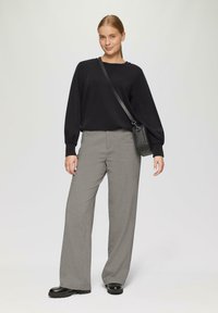 Zwart langemouwen trui, grijze wijde broek en zwarte schoenen. Verstelbare zwarte schoudertas met een gestructureerde afwerking.