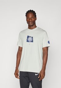 Ανοιχτό γκρι βαμβακερό t-shirt με γαλάζιο και λευκό λογότυπο μπροστά και γαλάζια πινελιά στον αριστερό μανίκι. Απλό σχέδιο με στρογγυλή λαιμόκοψη.