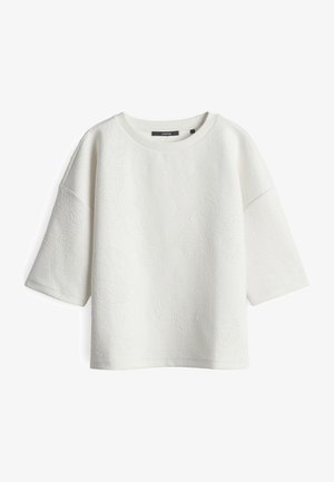 Top bianco a maniche corte con delicato motivo floreale in rilievo, scollatura rotonda e vestibilità morbida, mostrato su uno sfondo bianco.