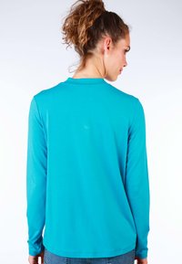 Langärmliges Oberteil aus türkisfarbenem Stoff, mit Rundhalsausschnitt und geradem Saum. Glatte Textur mit minimalen Designdetails.