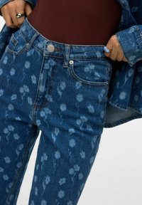 Niebieskie dżinsy z nadrukiem kwiatowym, z wysokim stanem, przednimi kieszeniami, kontrastowymi szwami i metalowym guzikiem do zapięcia.