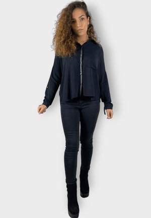 Sudadera corta de color navy con cremallera frontal y bolsillo; mangas largas, tejido suave, combinada con jeans negros ajustados y botas negras de tobillo.
