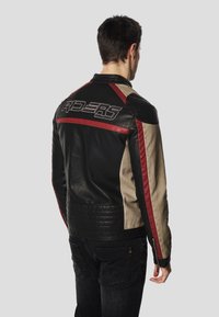 Black and beige leather jacket featuring red accents, ribbed texture at the waist, and "RIDERS" logo on the back in stylized lettering.